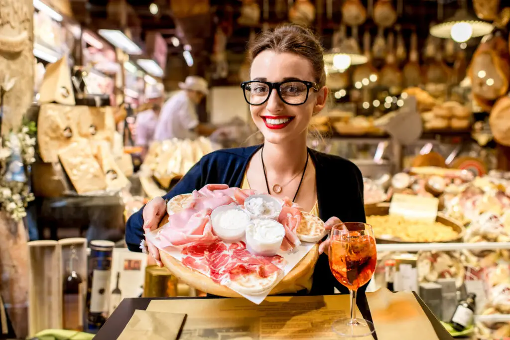 Young woman enjoying traditional Italian meats and cheeses at a local food shop on an Italy food tour