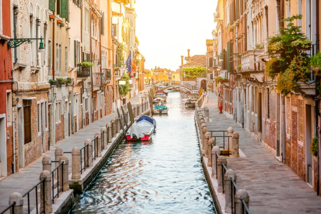Romantic small canal in Dorsoduro, Venice, Italy with historic buildings, boats and a stone bridge at sunset