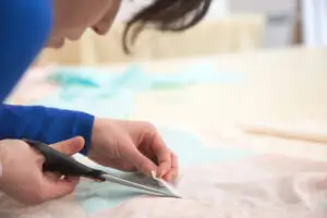 Young woman cutting fabric with scissors in an artisan tailoring atelier during an Italian craft workshop tour